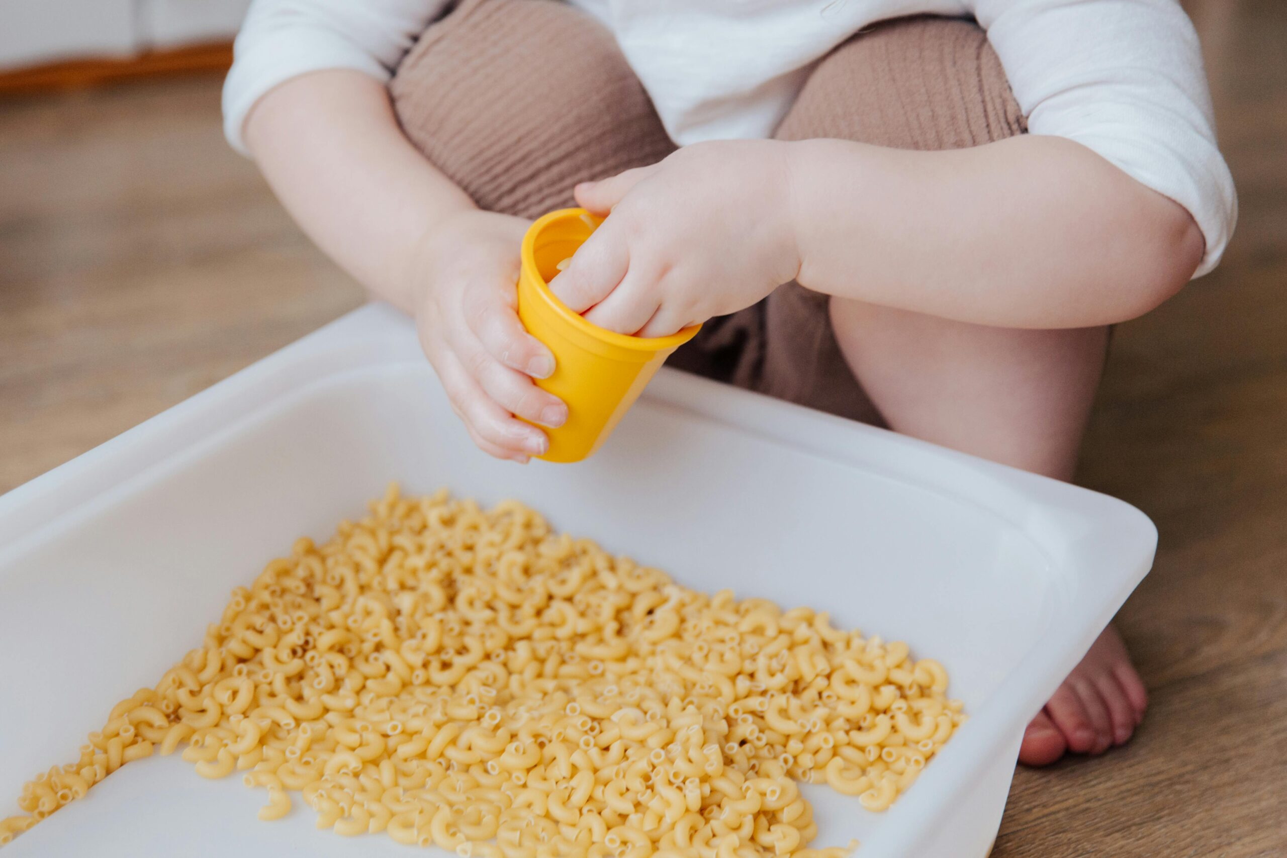 A young child plays with dry macaroni in a sensory activity, enhancing creativity and learning.